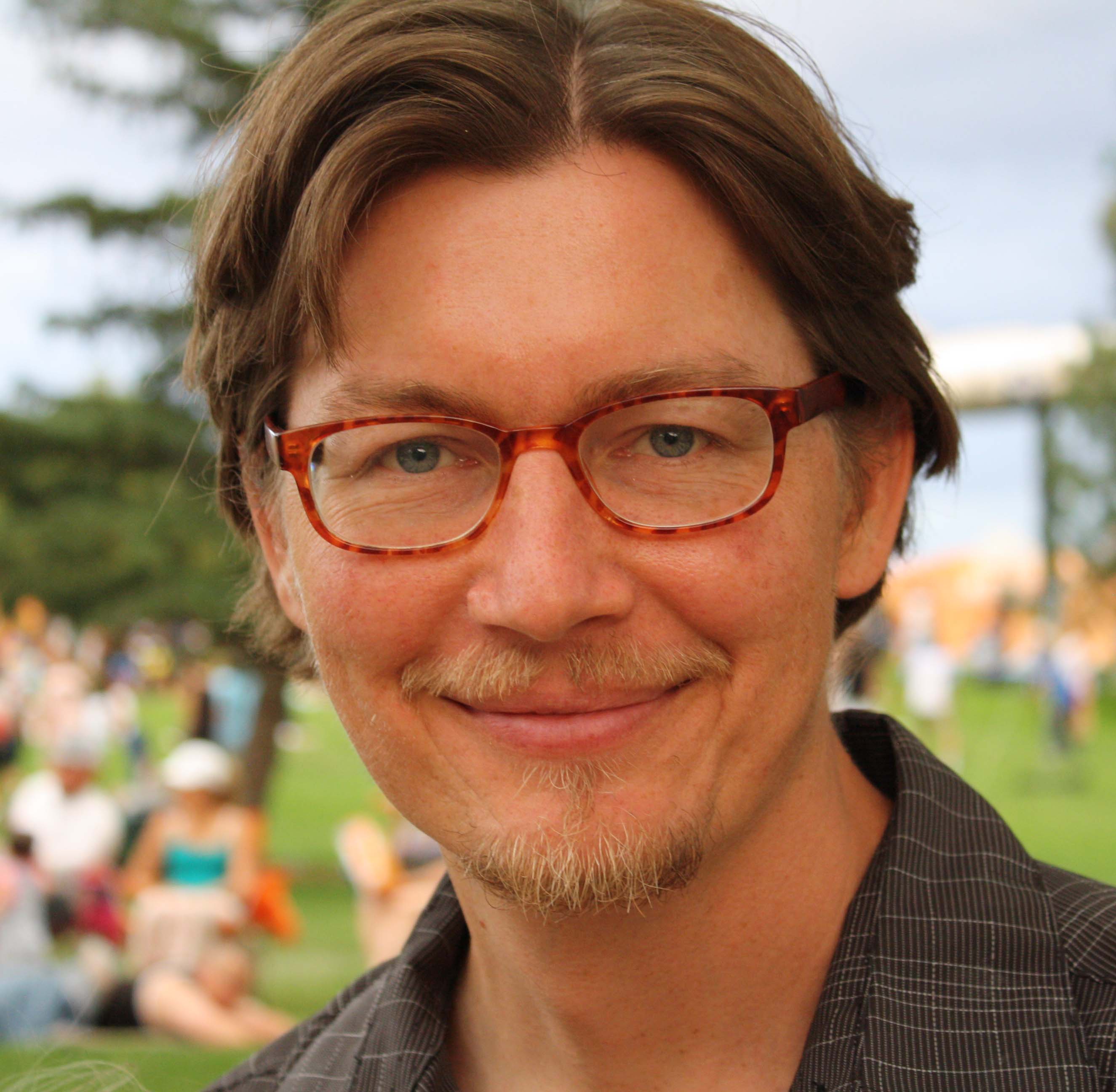 man with pale skin and glasses photographed from the neck up in an outdoor setting