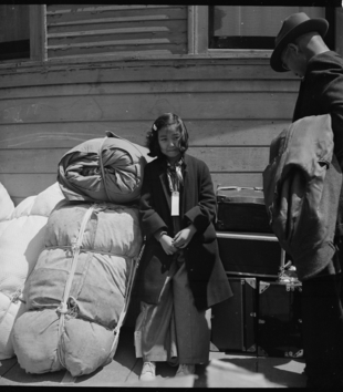 Black and white photograph of young Japanese American girl named Kimiko Kitagaki with luggage awaiting transportation to the Tanforan temporary detention Facility