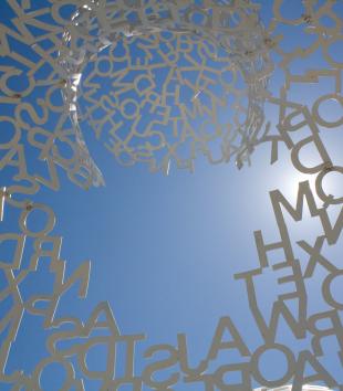 Blue sky with a silver sculpture of connected letters 
