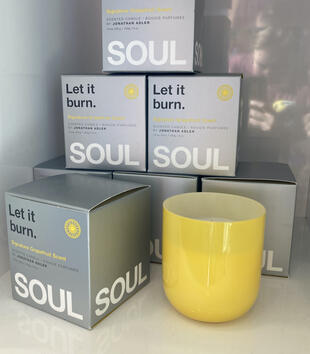 Stack of Jonathan Adler 'Soul' candles in their boxes stacked in a pyramid, with one unboxed candle on the right