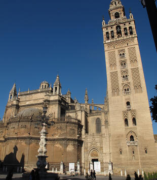 The view of a massive cathedral captures the exterior of the curved Capilla Real topped with a dome. A large bell tower rises off to the side and is decorated with geometric ornament.