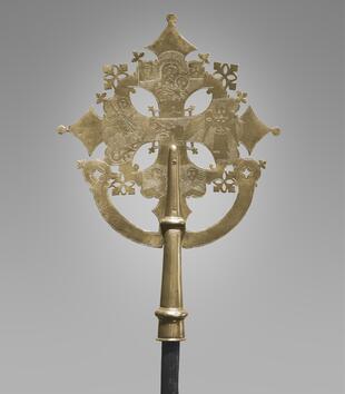 A gold pattée cross has flared arms that narrow at the center and are incised with low relief designs. Madonna and Child are depicted near the top and Saint George and the Dragon is represented on one of the arms.