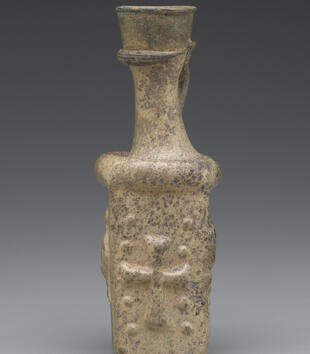 A four-sided glass jug with a narrow neck is decorated with Christian motifs. This side depicts a cross. A protruding ring runs around the jug at the base of the neck. 