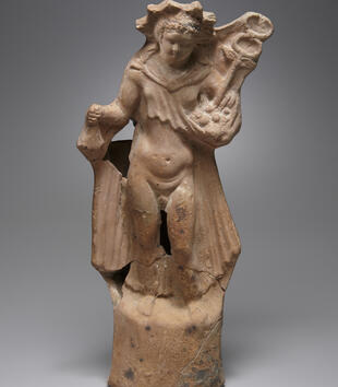 A terracotta sculpture depicts Hermes as an adolescent, naked, and with a slightly pudgy stomach. He holds a staff with wings and two snakes atop it. He wears a flowing cloak down his back and a star-shaped crown. 