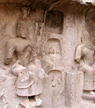 Two enthroned figures are carved in high-relief on a light-colored slab of stone. Parts of their faces and bodies have fallen away. They wear long robes delineated by a incised lines of drapery. One figure's face has plump lips and a placid expression.
