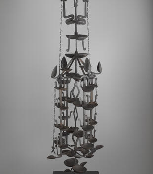An intricate iron oil lamp has forty-six cups affixed to five shafts, which are arranged in a circle and create a tree-like shape. There are decorative volutes on top that abstractly recall two ram's horns. 