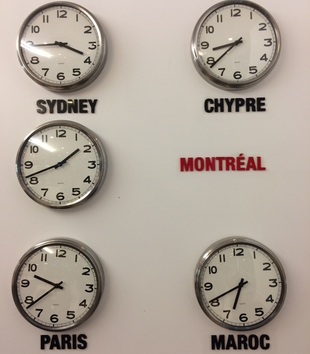 Clocks hung on a white wall displaying the times of various time zones