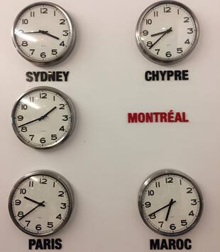 Clocks hung on a white wall displaying the times of various time zones