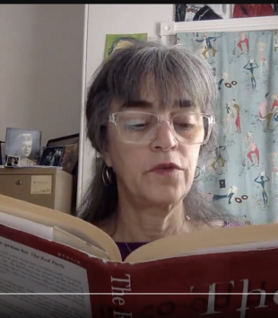 Dr. Levitt pictured, shoulders up, in a purple shirt and glasses, reading from Maggie Nelson's The Red Parts from her office.