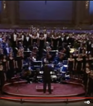 A stil from a YouTube video features a choir, symphony orchestra, and conductor on the Carnegie Hall stage