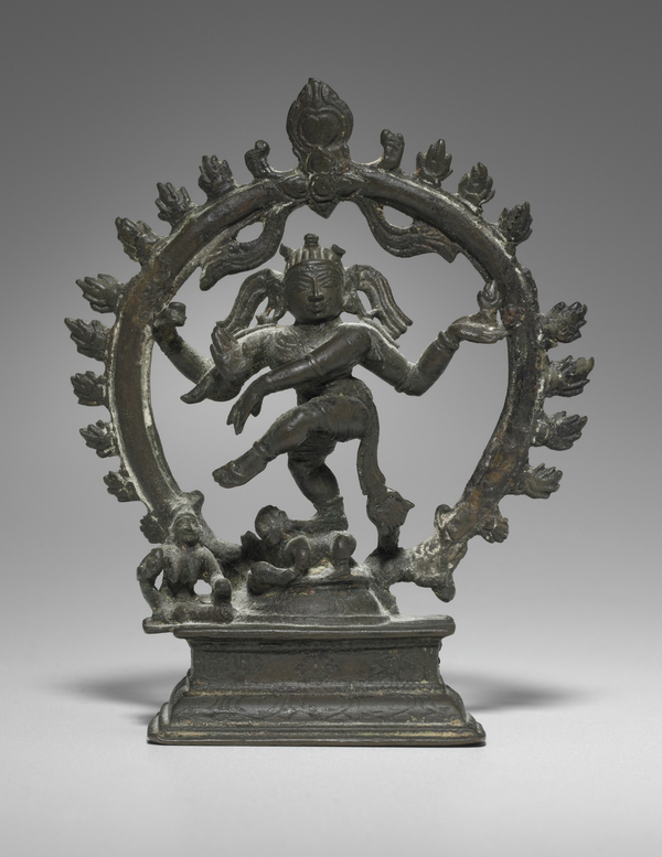 A bronze figure with many arms gestures with his hands and lifts his leg in dance. He is encircled by a ring of flames and stands on a smaller figure. His expression is calm with a slight smile.