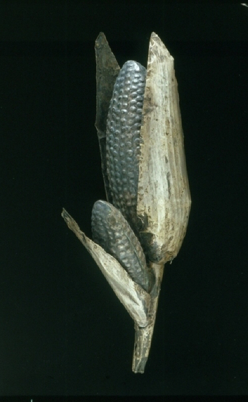 A detailed hammered corn statue depicts a smaller ear of kerneled corn projecting from the base of a larger ear of corn.