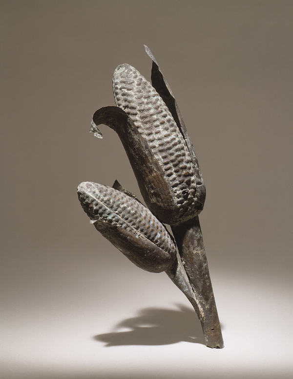 A hammered silver sculpture depicts two ears of corn with delineated kernels and slighly curling leaves.