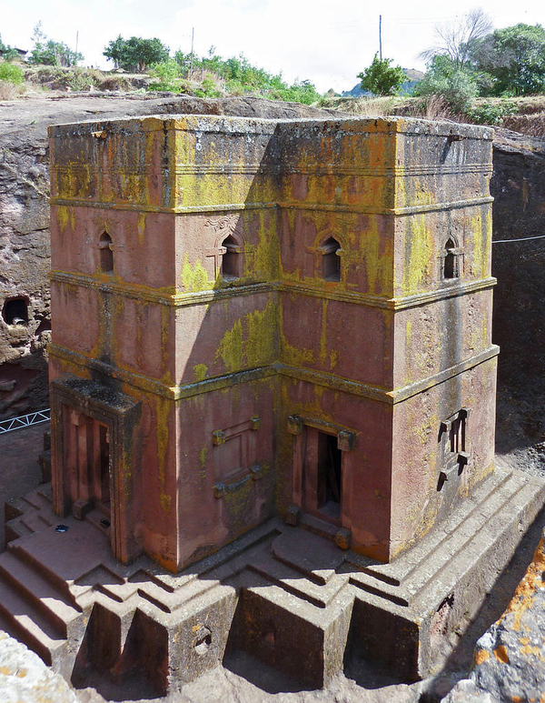 A rock-hewn monolithic church of red volcanic tuff is carved down into a massive rock. Just a corner of its cruciform plan is visible, and the straight walls are further chiseled out into windows on the upper storey and doors on the lower level. 