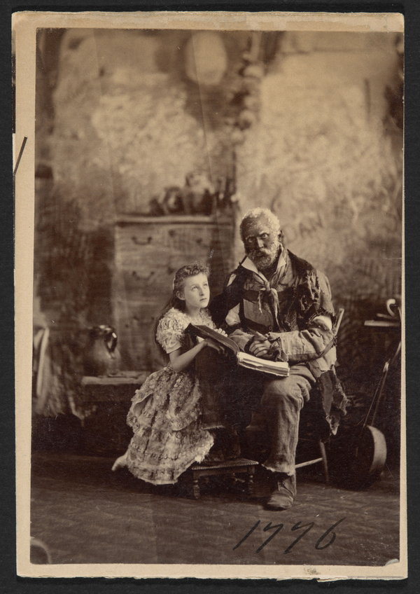 A sepia photograph depicts a young white girl in a flouncy dress kneeling beside a seated black man in ragged clothes. The two hold a book open on the black man's lap. Simple furniture and other household items lie in the background.