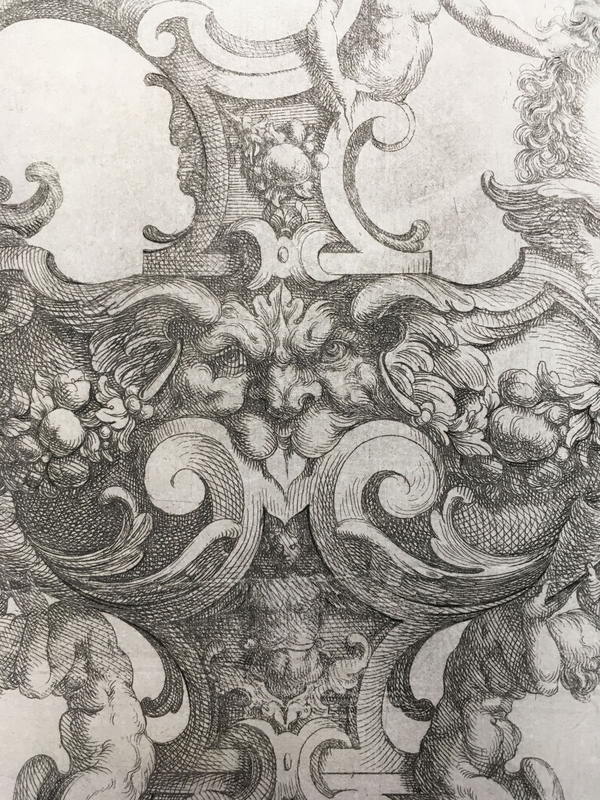 A fantastical etching depicts a central grotesque head with flaring nostrils and a stuck out tongue. It is surrounded by swirling volutes, small fruits, and muscular nudes.  
