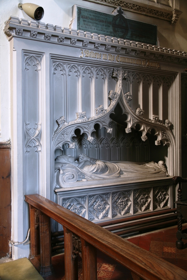 The parting marble curtains of a square canopy tomb reveal the marble effigy of a woman laying on a carved cushion.