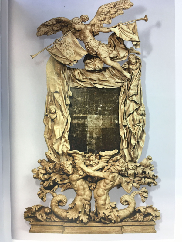 A gilt silver mirror frame depicts folds of fabric in which putti are embedded. The frame is held up by two marine creatures with flambeaux and is topped by an angel with two fanfare trumpets.