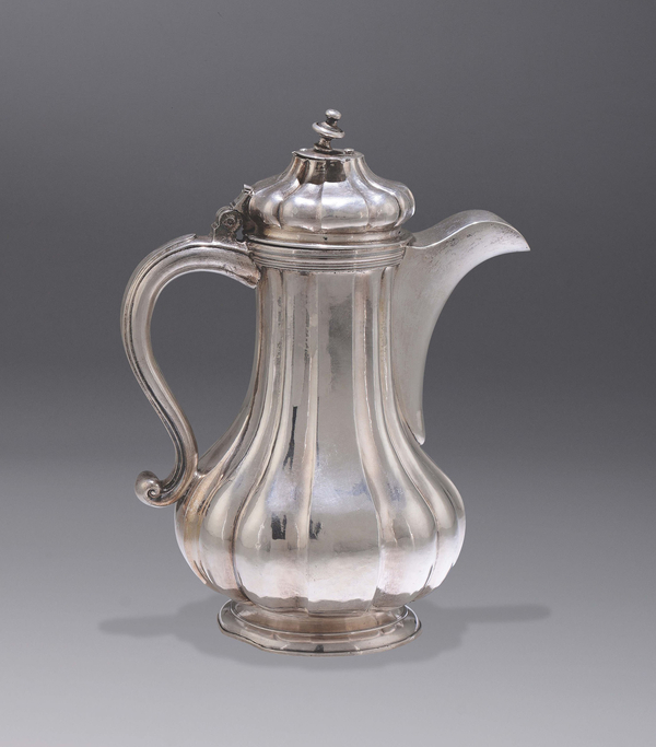 A silver jug for hot chocolate has a volute handle, round cap, fluted body, and a pouring spout.