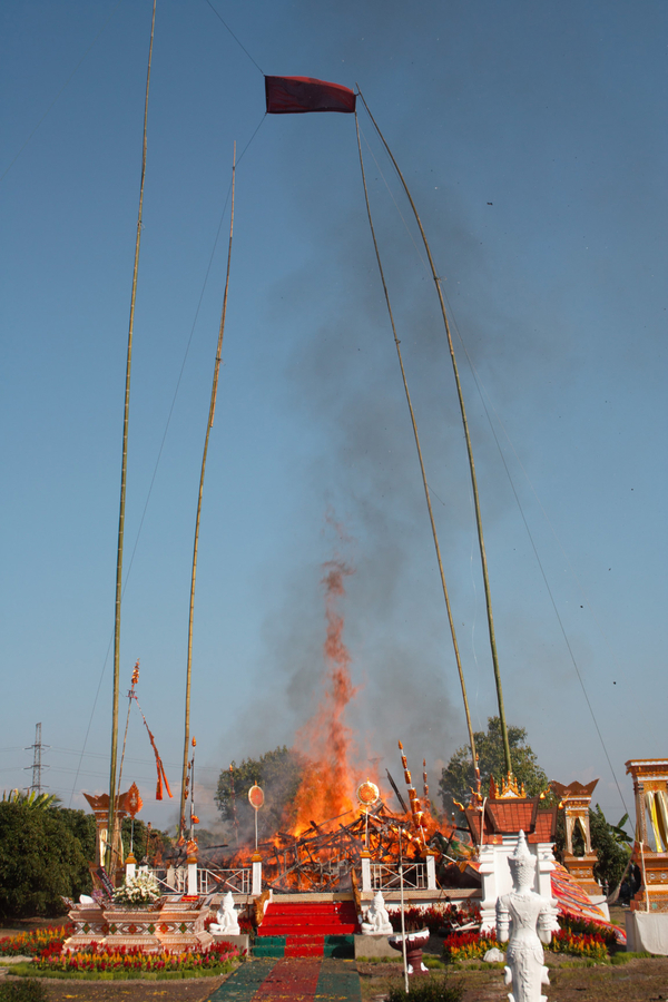 Smoke floats up from the pile of burning materials left behind on a platform following the burning of a prasat sop cremation structure. 