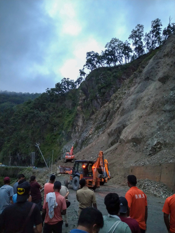 People gather around two orange backhoes as they work on the side of mountain. A landslide has removed this face of the slope.