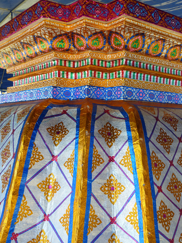 A detail of a cremation structure focuses on its embellished surface. Colorful paint and foil applied in geometric and floral patterns give it a shiny, decorative surface.