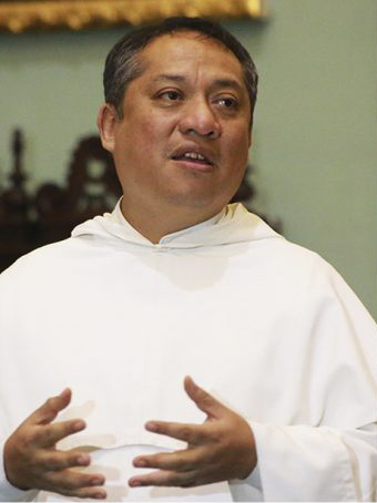 In this close-up photo, a Latino man in the white robes opens his mouth and gestures with his hands as if speaking.