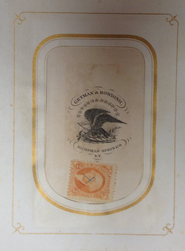A gold-bordered book page is printed with a black-and-white eagle beneath an arc of stars. Text reads "Getman & Bowdish" above and "Richfield Springs NY" below. A stamp is affixed beneath the print.  