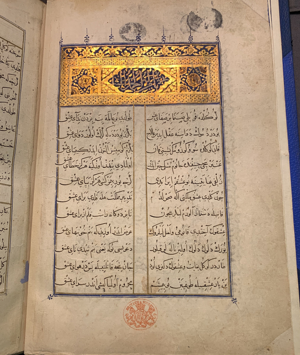 An illuminated Islamic text is open to a page with two columns of Arabic calligraphy topped by a shining golden header.