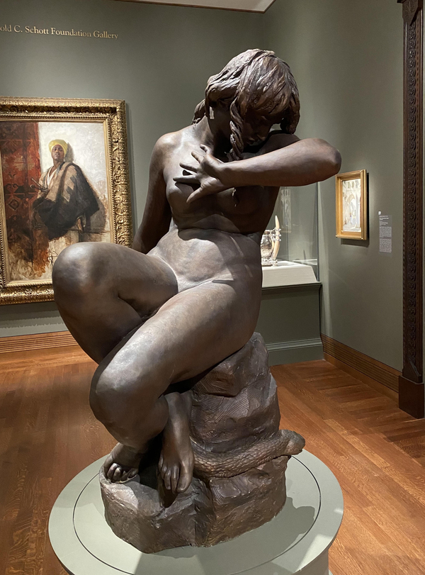 In a naturalistic, nude bronze, Eve averts her face in the crook of her arm and crosses her legs awkwardly. At her feet, a serpent coils menacingly around a rock upon which Eve cowers.