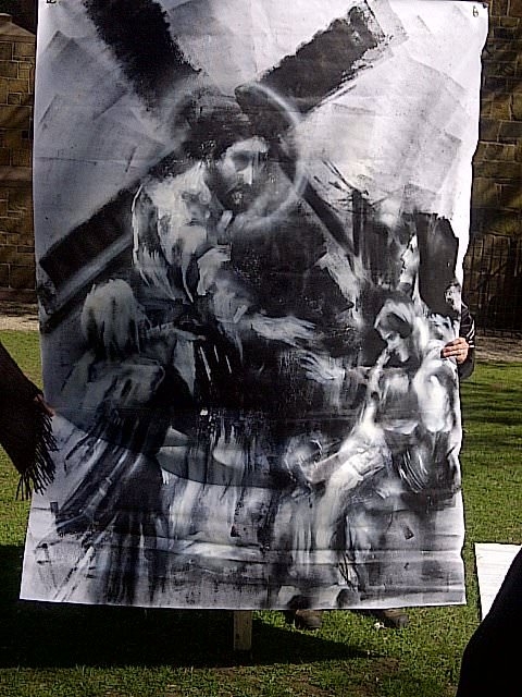 Two hands outstretch a white canvas with a black spray painted image of Jesus carrying the cross.  