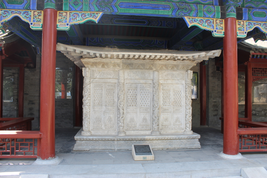 Tomb monument in white stone with elongated top, set behind two red columns