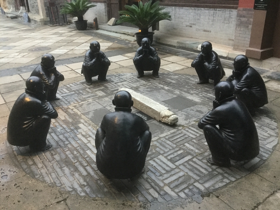 photograph of a sculpture of eight male figures crouched in a circle on a stone circle