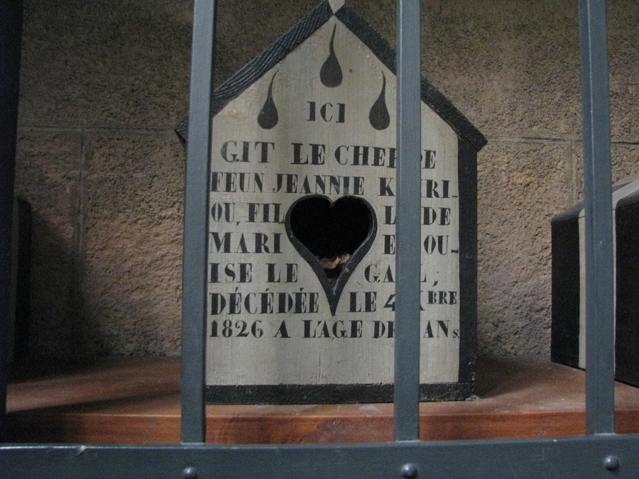 A white, house-shaped box with black inscriptions on the front is visible through black bars. There is a heart-shaped opening on the front.