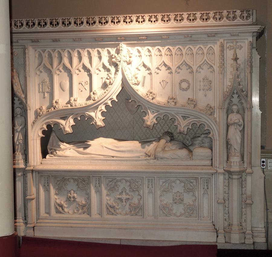 A grand, ornate tomb consists of a marble canopy erected above a marble tomb-chest. A marble effigy laid atop the chest can be viewed through decorative marble curtains on the canopy.