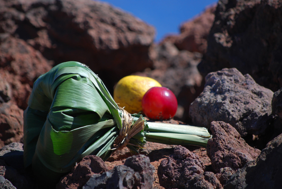 A tied bundle of green leaves lies on a rocky landing alongside two colorful pieces of fruit.