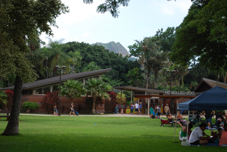 People gather around a building complex situated in a lush landscape and labeled "Honolulu Zoo."
