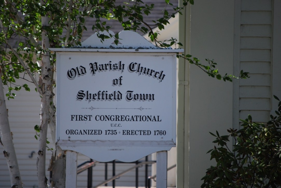 A white wooden sign with black text reads, "Old Parish Church of Sheffield Town. First Congregational U.C.C. Organized 1735. Erected 1760."