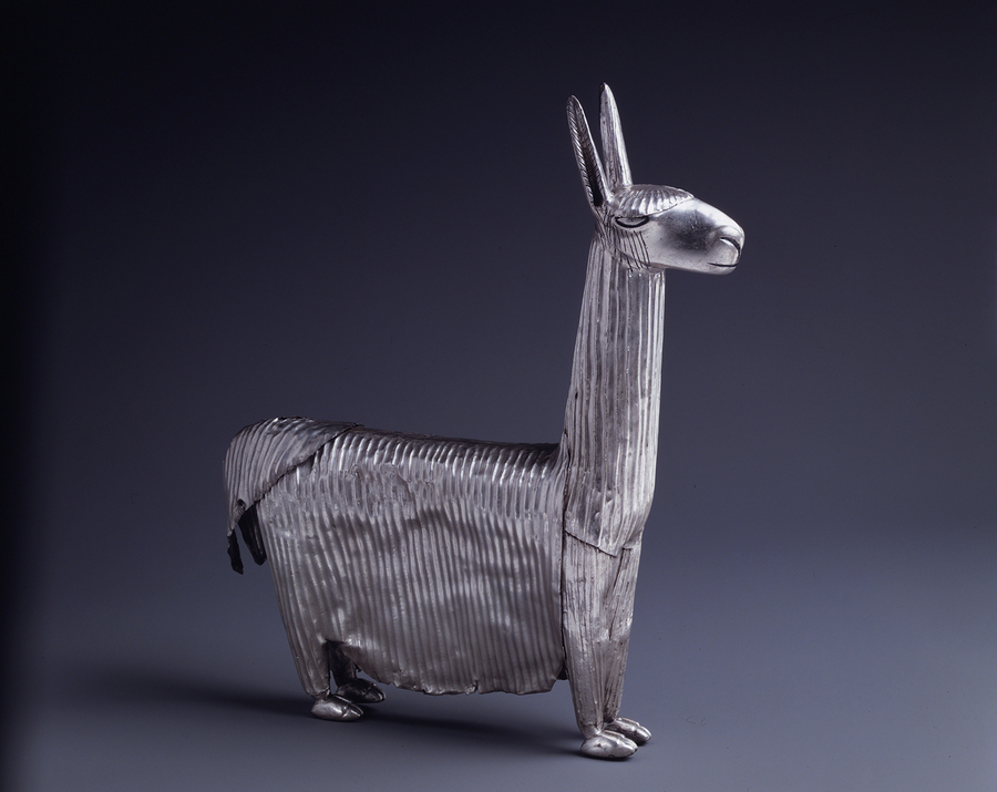 The long coat of wool on a llama figurine is conveyed by vertical lines on the metal sheets of its body. A patch of metal hair just slightly covers its almond eyes. The rest of its head is smooth.
