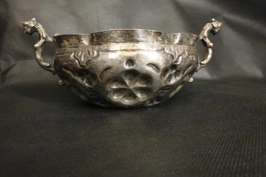 A small silver cup has handles on either end. It has a fluted lip and is embossed with a lobed design.