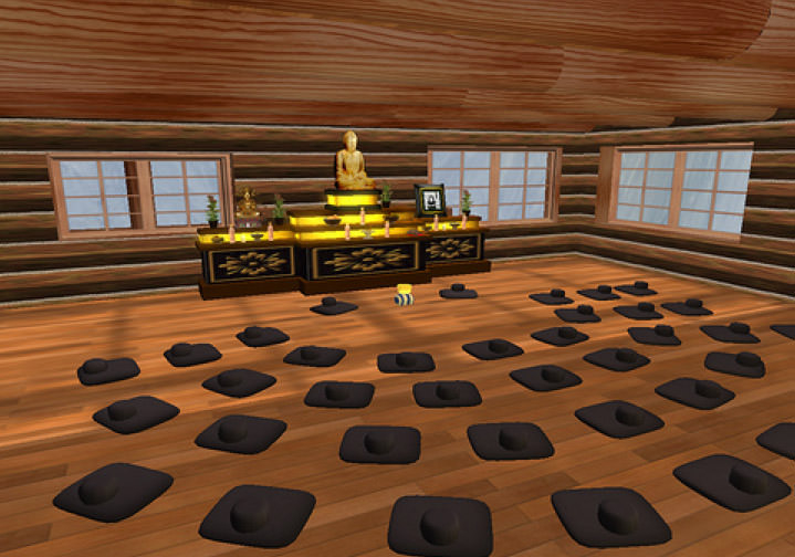 In this slightly pixelated digital image, rows of black cushions lay around a glowing black and yellow altar. The altar has a statue of buddha atop it.