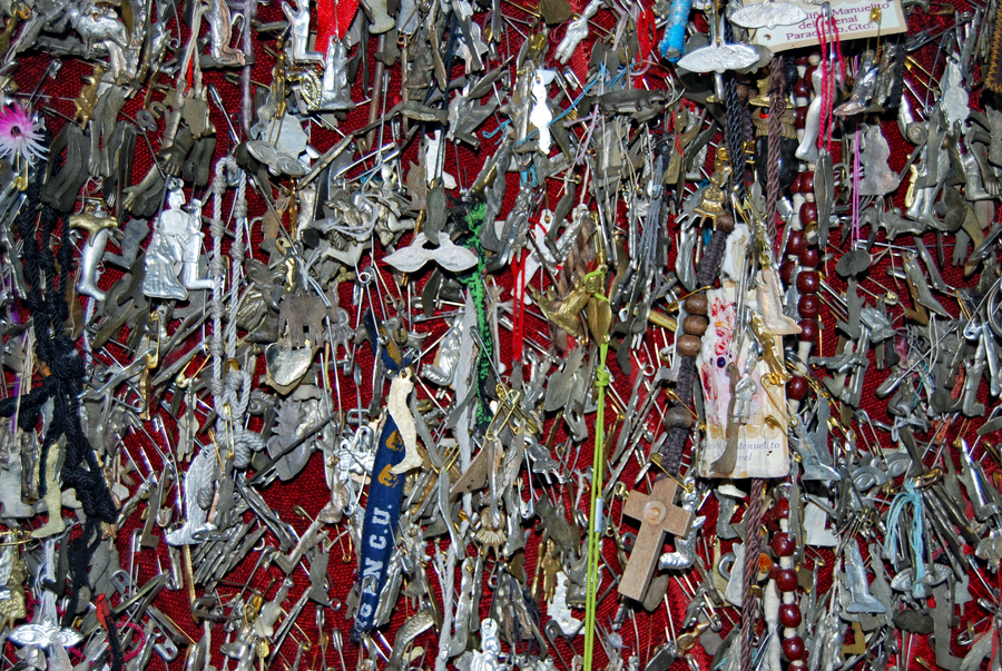 A range of numerous metal milagritos hanging on a red wall