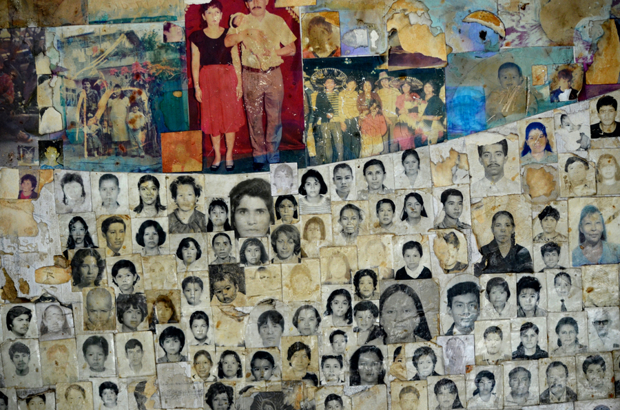 Wall collage consisting of black and white passport style photographs of individuals and coloured family photos