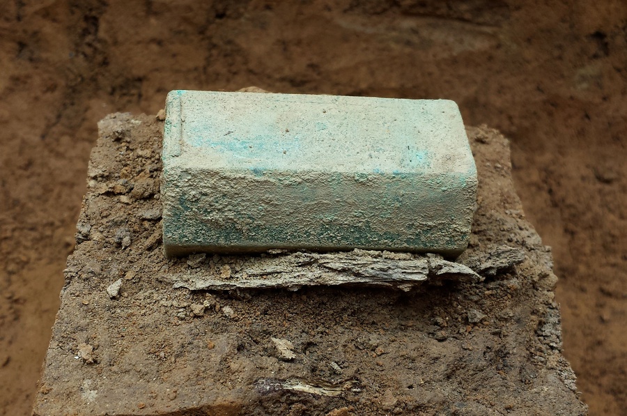 A soil-covered and slightly green rectangular object rests on a patch of soil and rocks.