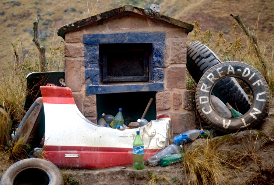 Shrine that looks like a small house, with ephemera such as tires and plastic bottles surrounding it