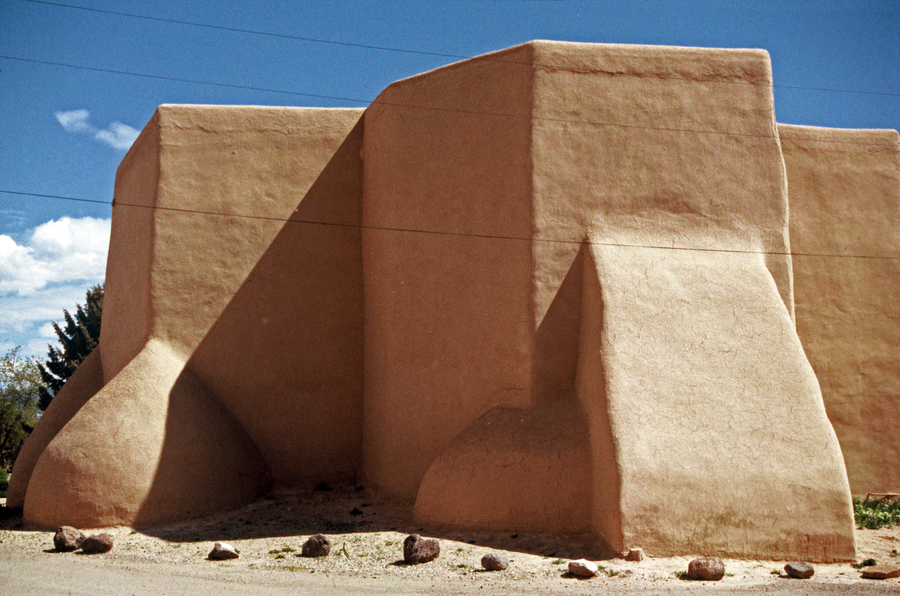 The peachy, adobe church's rear, with its large beehive-curved buttresses protruding from tall rectangular walls, appears sculptural in this close-up angle of the church.