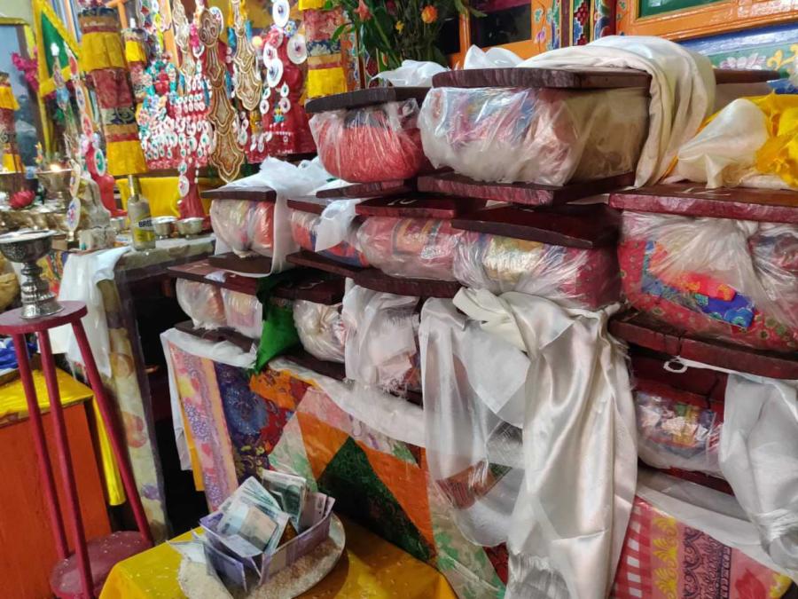 A table in a colorful household shrine is stacked high with books wrapped in bright scarves and plastic and stored between slabs of wood. 