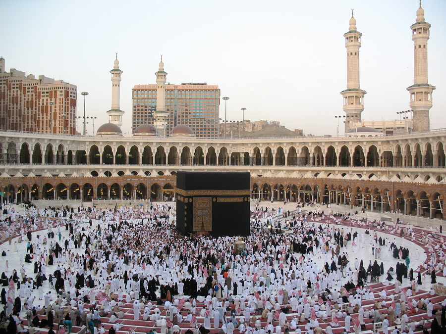 A photograph shows the gathering of white-robed worshippers around the large black box of the Kaaba. The box is covered with an embroidered black and silk curtain. A colonnade and four minarets are visible at the site.