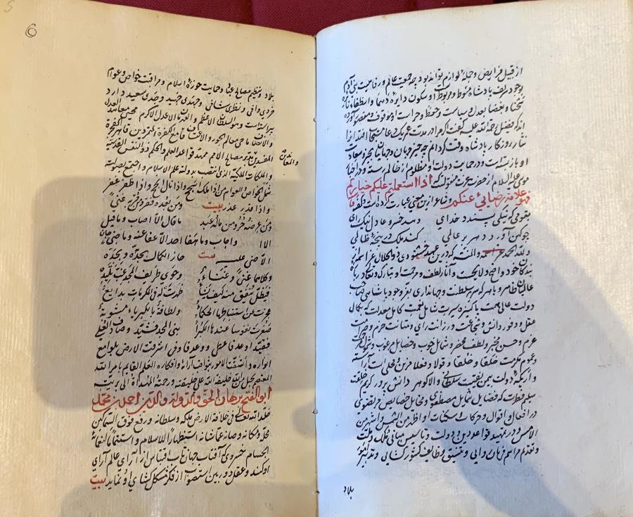 An illuminated Islamic manuscript is open to a spread of black Arabic calligraphy with some red details.