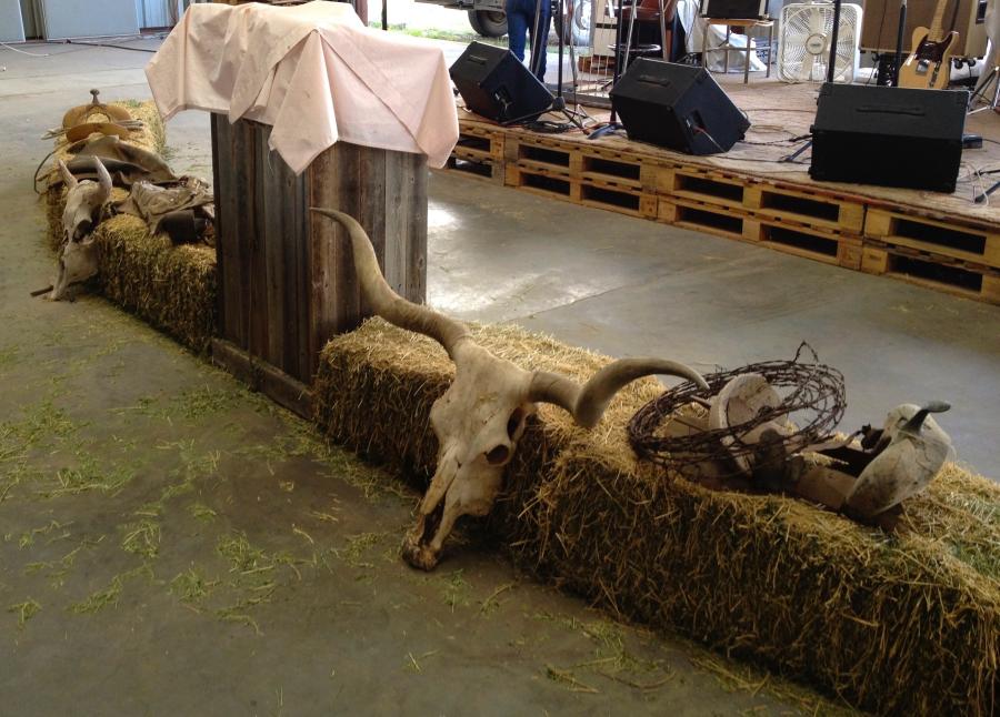 Horned cow skulls and saddles lie on top of the hay bales that line a simple pulpit within an assembly hall church.